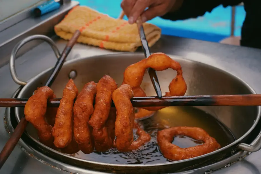 Picarones hang on a wooden stick over a pan of hot oil at a street cart