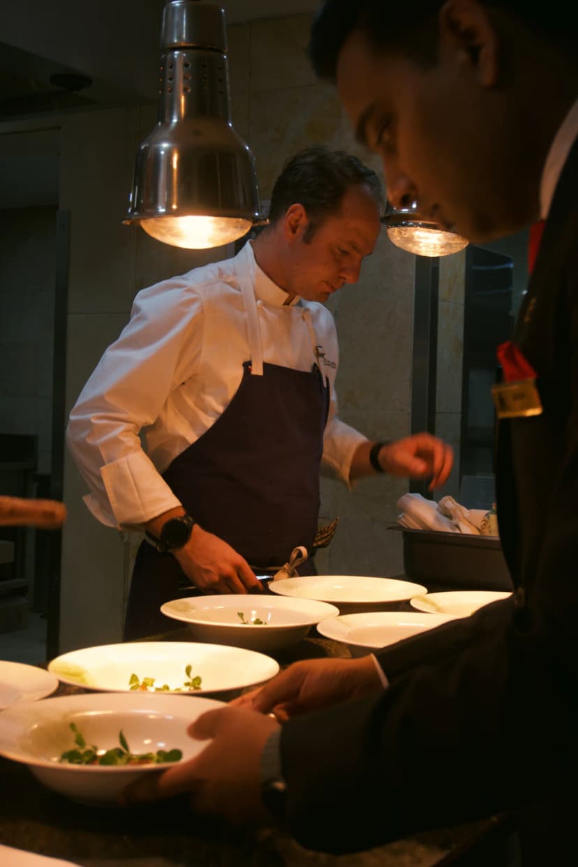 Chefs working together under heat lamps at the kitchen pass in Bengaluru