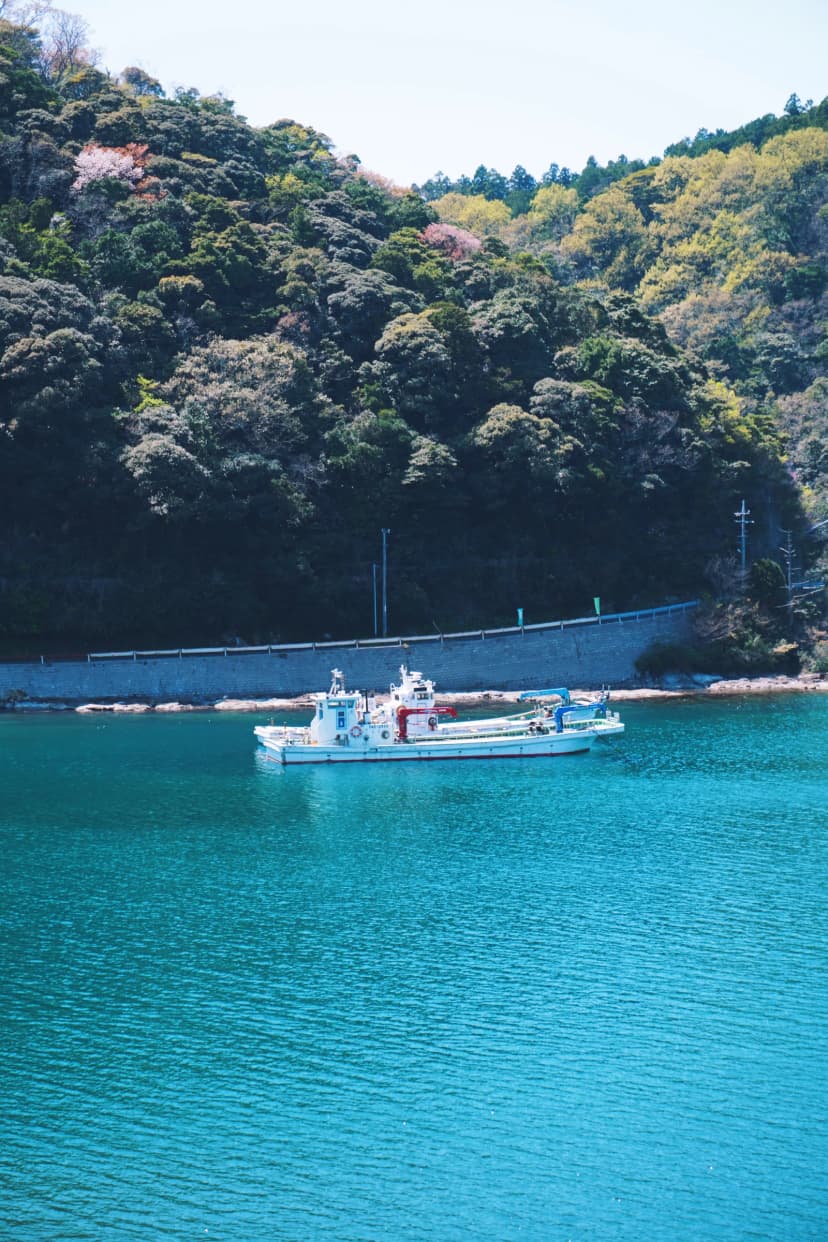 A small boat on turquoise water below wooded hills in Japan