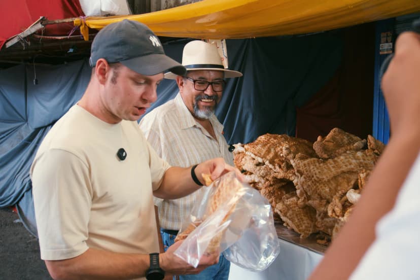 Jason tasting food beside Paco at a Mexico City market stall