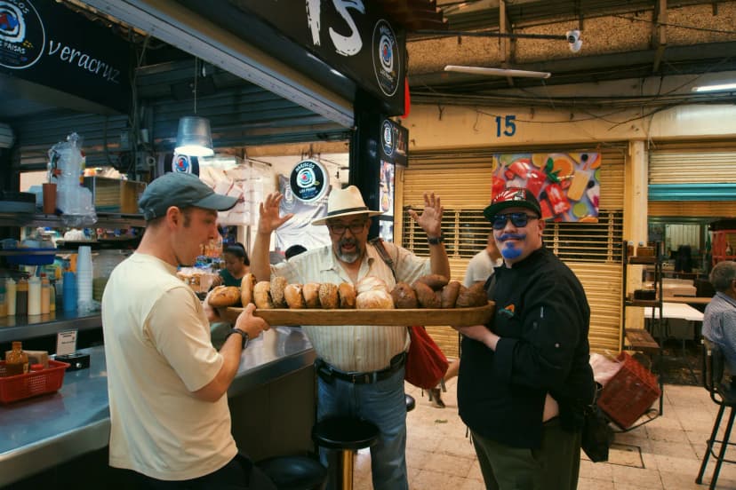 Jason and two men holding a long board of tortas at a market food counter