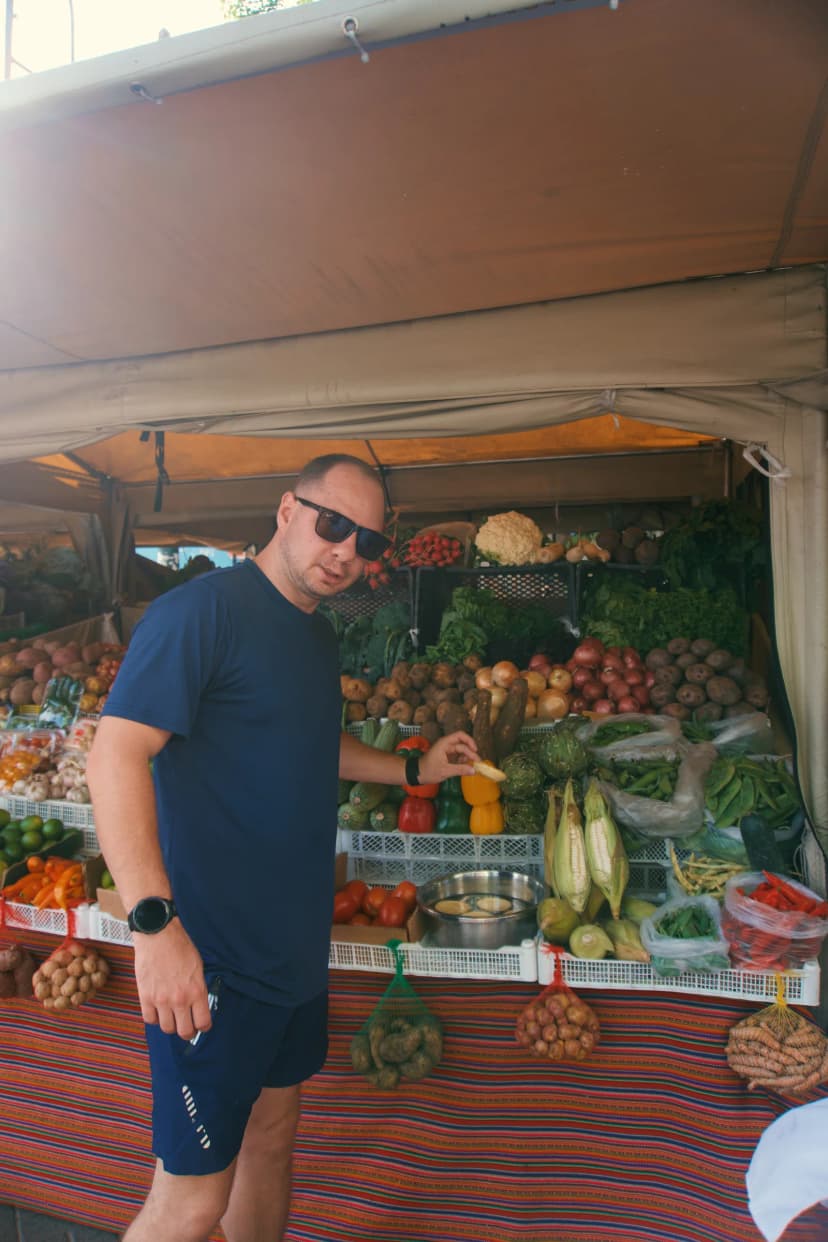 Jason beside a produce stall stacked with fruit and vegetables in Peru
