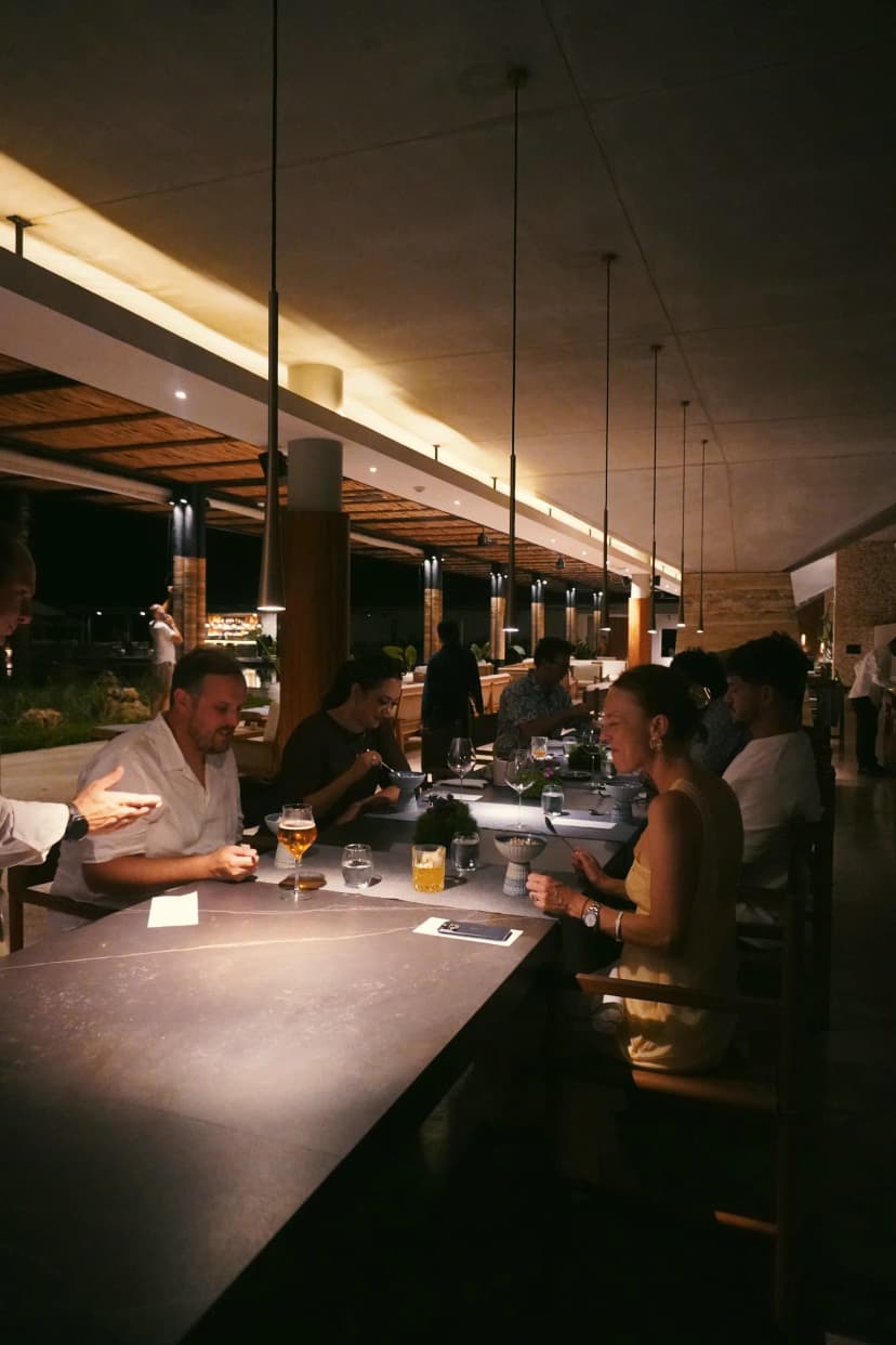 Guests eating at a long counter beneath pendant lights at Cap Karoso